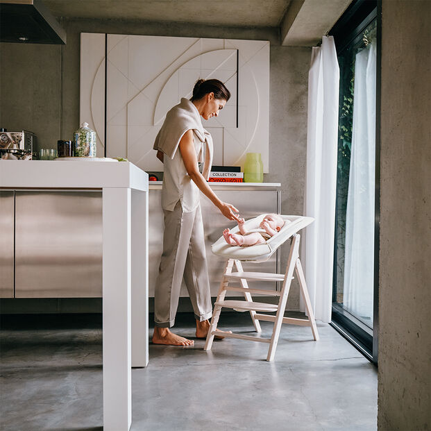 A woman stands in a modern kitchen interacting with a baby seated in a Click and Fold high chair.