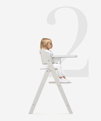 A child sits in a white Click and Fold high chair against a large grey background with the number two.