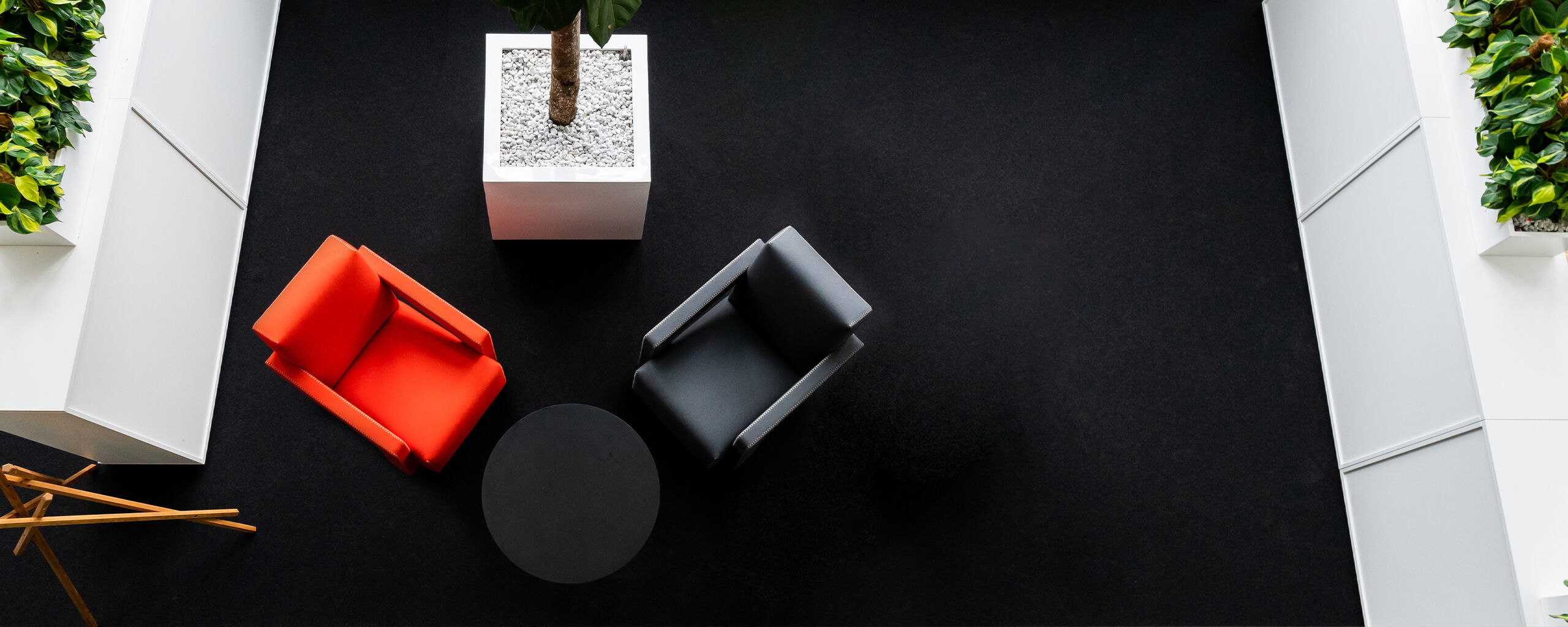 A modern waiting area with a red and a grey armchair, a round table, and a large plant pot.