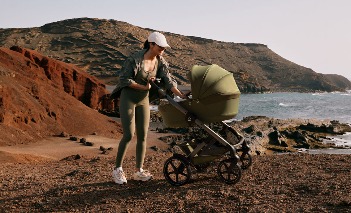 Eine Mutter in einem sportlichen Outfit, die nach ihrem Kind in der Talos S Lux Babywanne sieht.