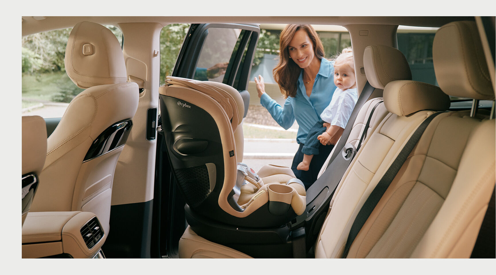 Woman holding a child stands next to a car with a Callisto G 360 rotating convertible car seat.
