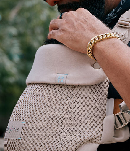 A close up of a man with his hand on top of his child's head. The baby is in an Amya baby carrier.