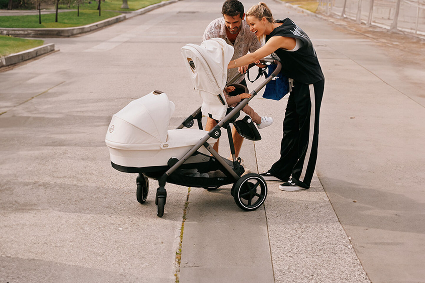 A couple smiling and leaning over a white pram on a pavement.