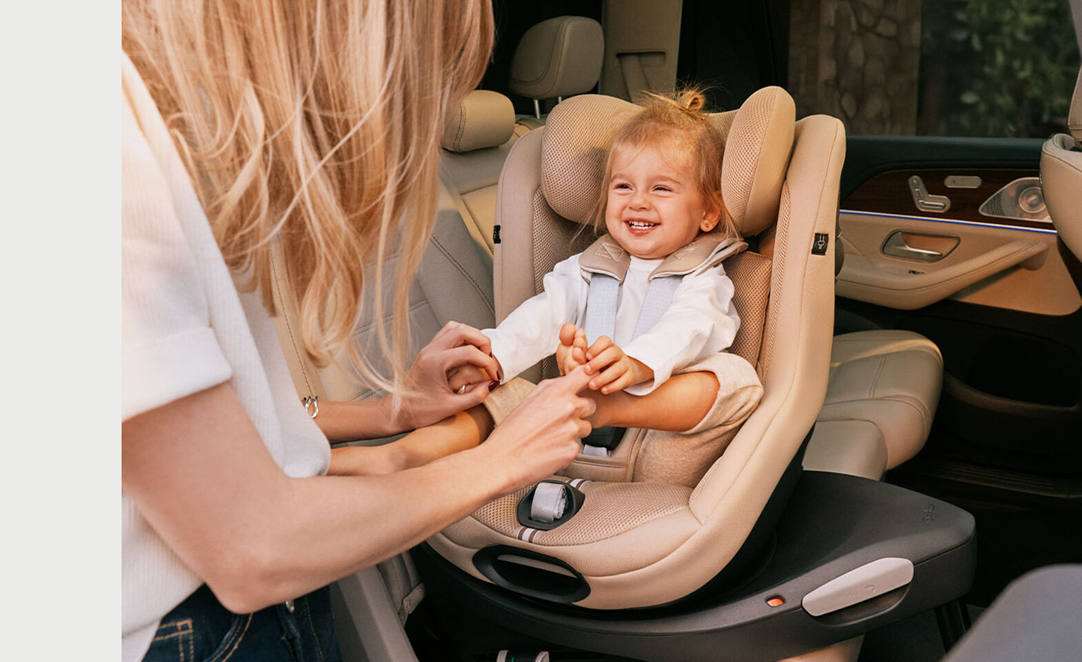 Woman tickling her daughter sitting in a Sirona G i-Size car seat. The car seat is rotated towards the door, the daughter is laughing.