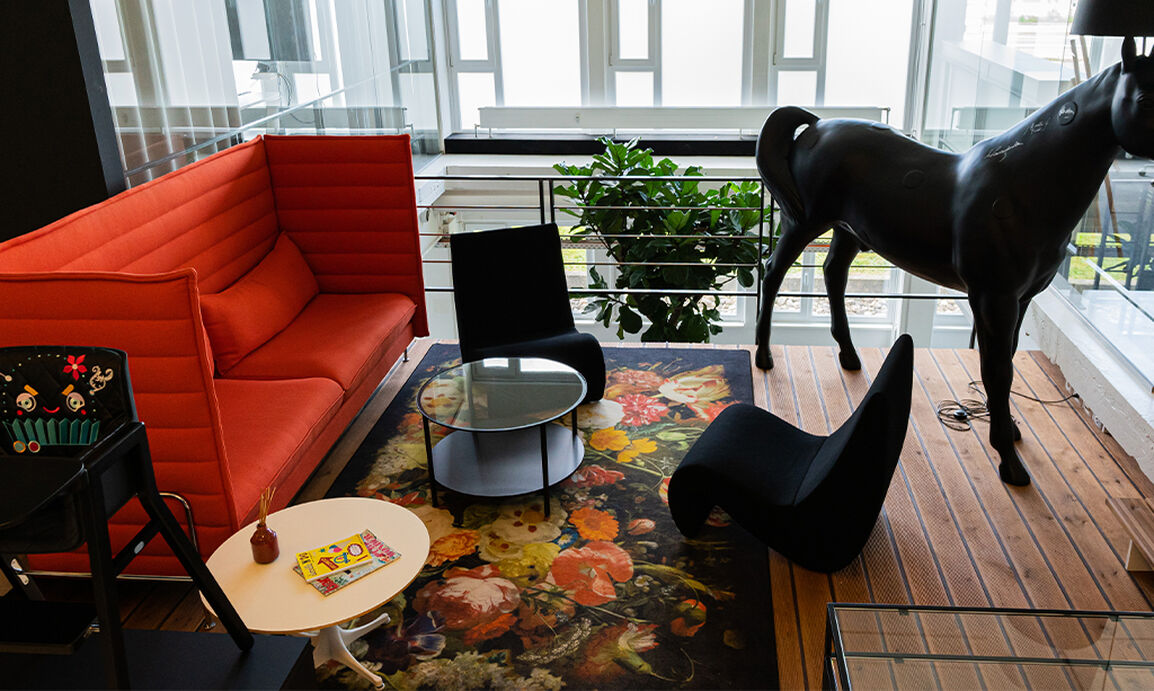 A modern living room with a red sofa, floral rug, black chairs, and a large black horse sculpture.