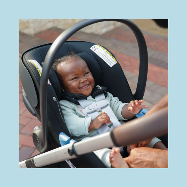 A smiling baby is seated in an Aton G Swivel car seat.