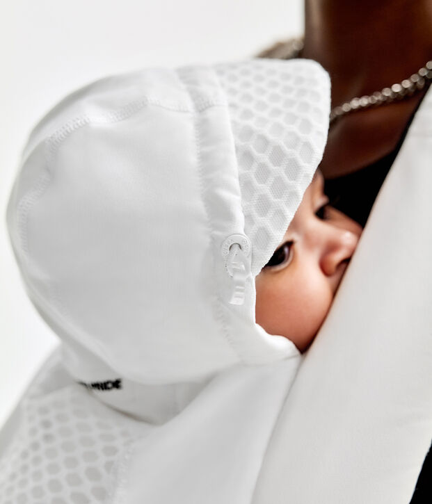 A baby in white clothing cradled in someone's arms.