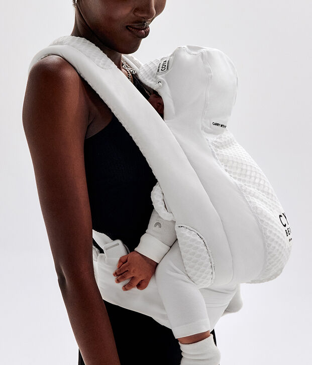 Woman carrying a baby in a white baby carrier.
