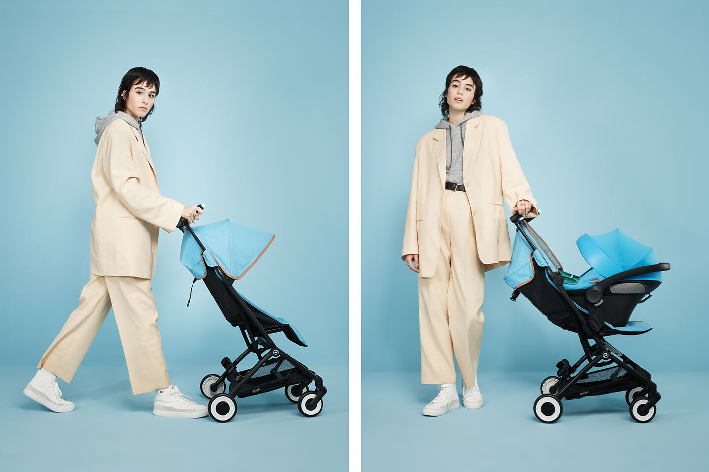 Woman in beige suit with grey hoodie pushing a blue Libelle, the smallest fold stroller, against a blue background.