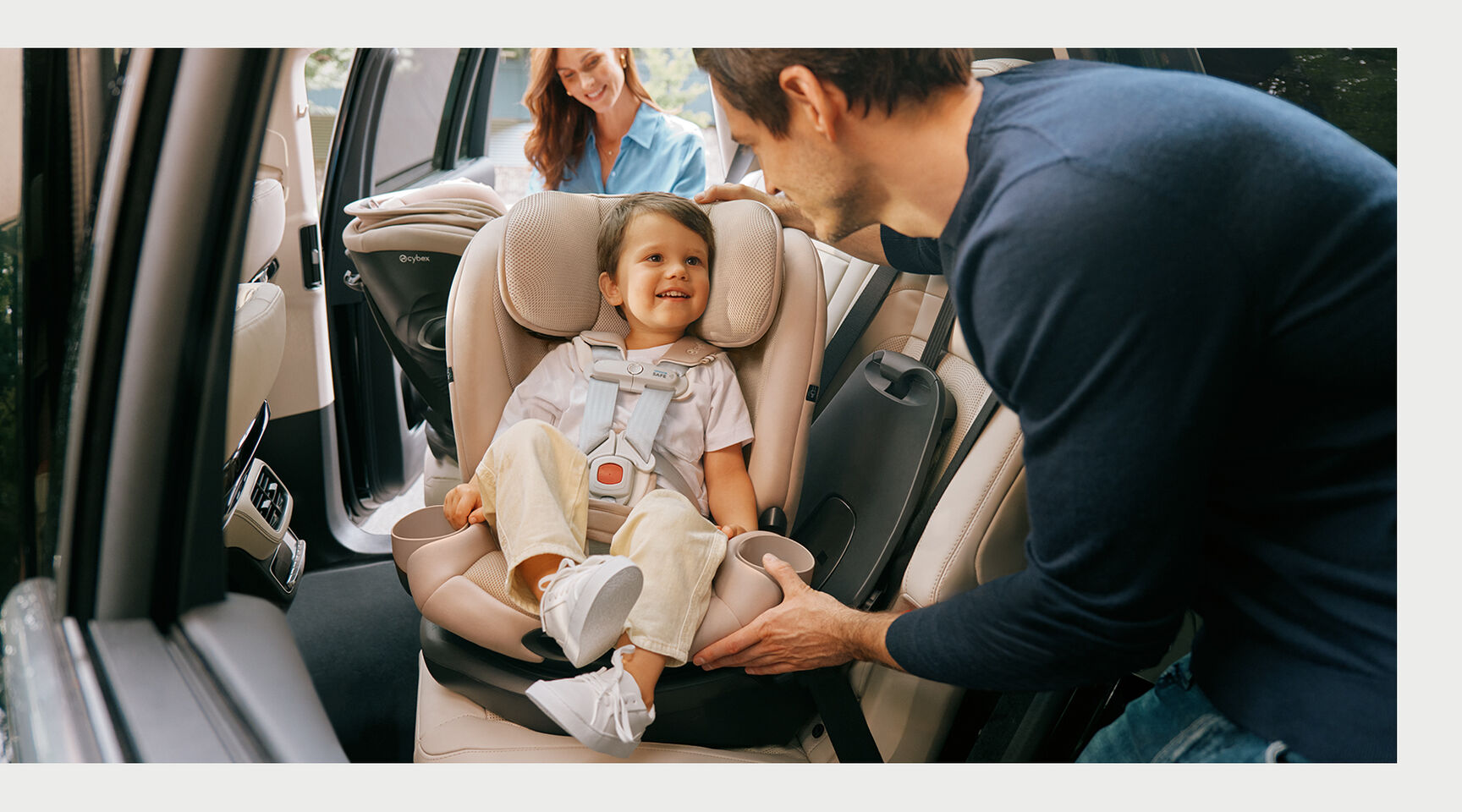 A child sits happily in a Callisto G 360 rotating convertible car seat in a car while an adult adjusts the seat.