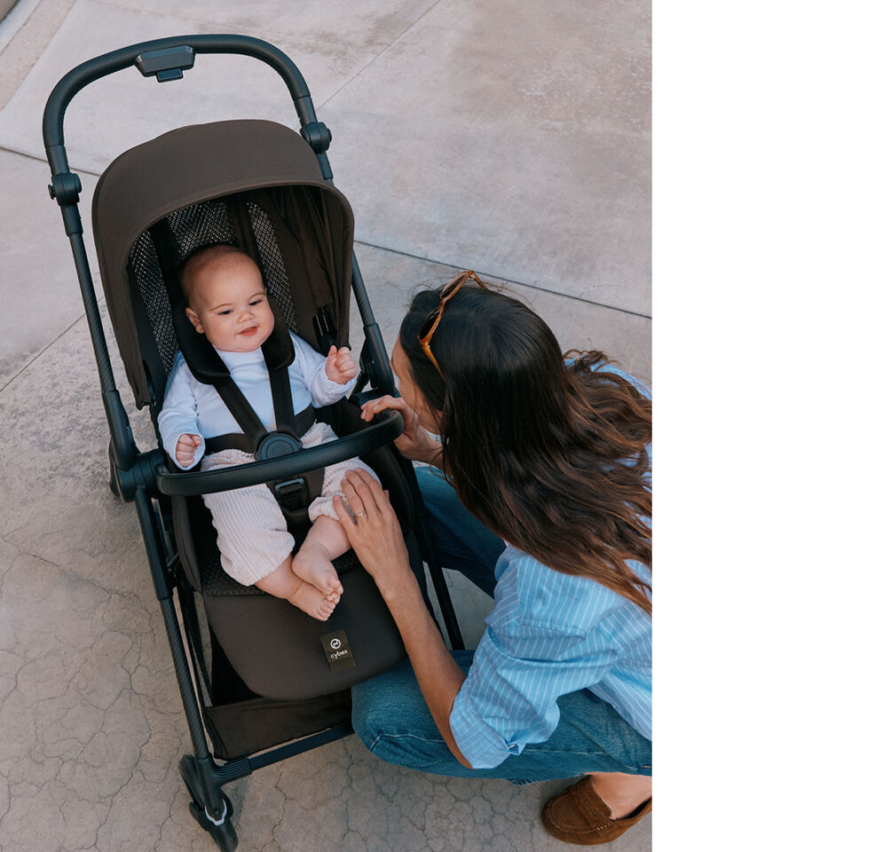 Un bambino &egrave; seduto su un passeggino leggero Melio Carbon mentre una mano allaccia la cintura di sicurezza.