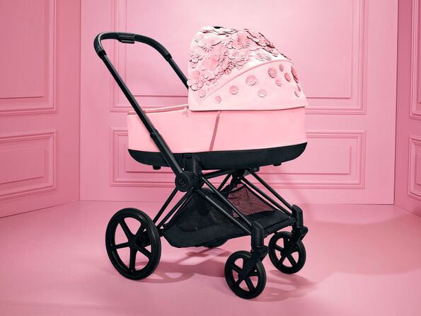 CYBEX Simply Flowers barnvagn i rosa med blommiga dekorationer mot en rosa bakgrund.