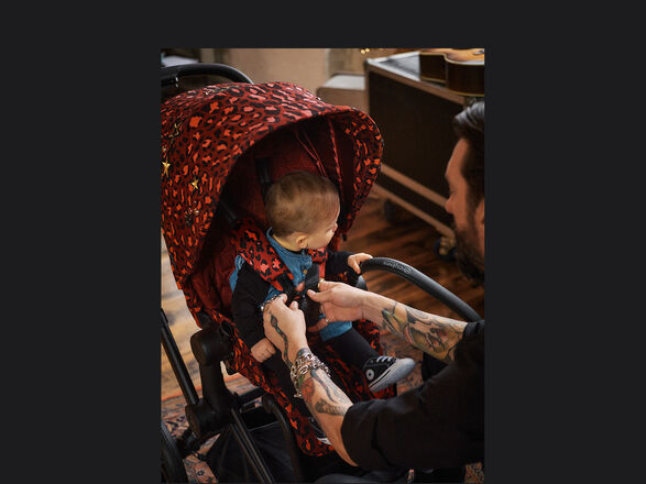 A man buckling a baby into a CYBEX Rockstar pushchair with a red leopard print.