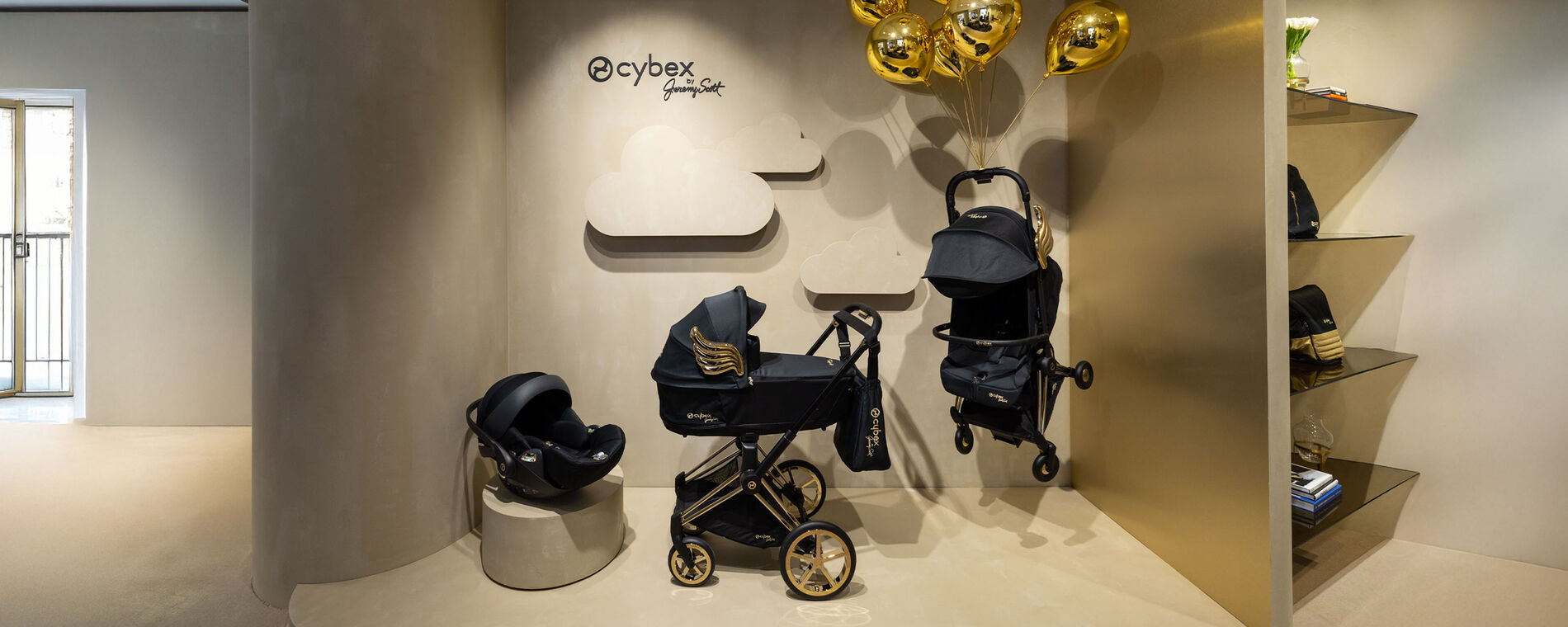CYBEX by Jeremy Scott &lsquo;Wings&rsquo; collection with golden balloons, stylishly displayed against a beige wall.