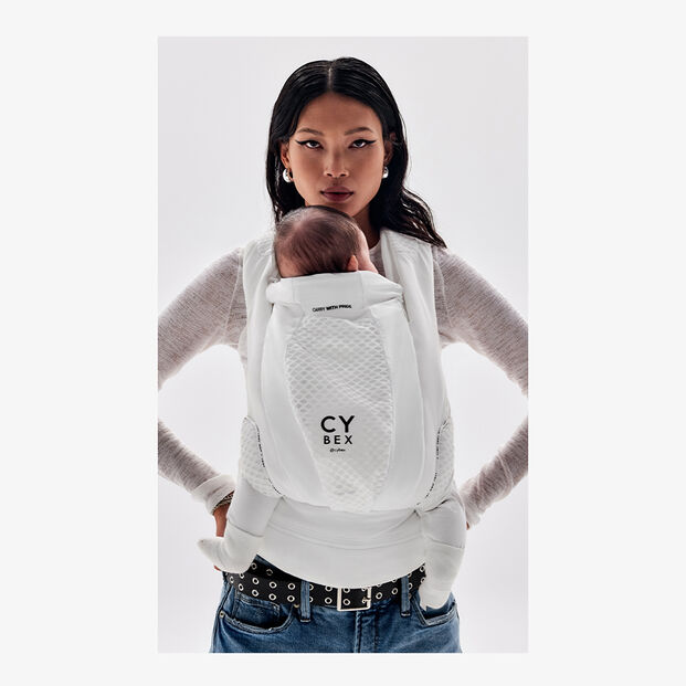 Woman carrying a baby in a white Cybex baby carrier.
