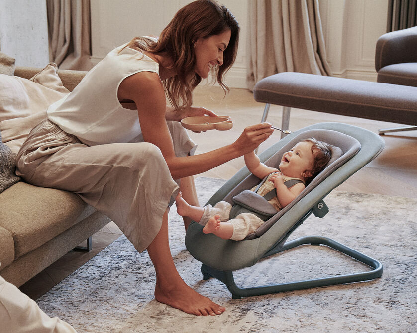 Mother feeding her baby sitting in a Bouncer baby bouncer.