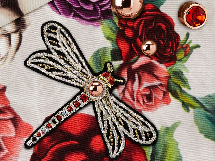 An embroidered dragonfly on CYBEX Spring Blossom fabric with a rose pattern and gold buttons.