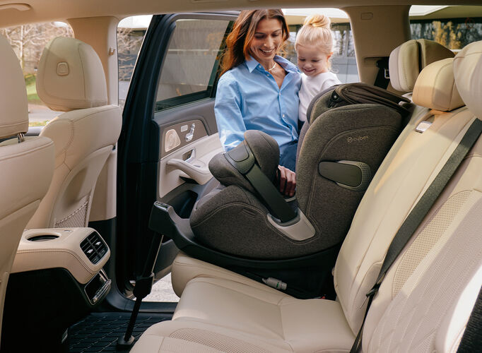 A woman holding her child and both smiling as she's about to put her child in her Anoris T2 i-Size car seat.
