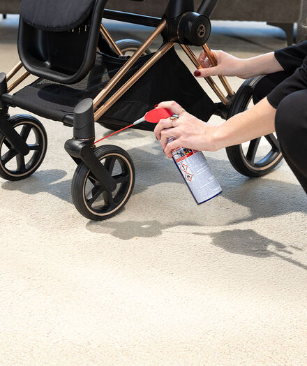 A woman with rings on her fingers spraying something at the wheels of a CYBEX stroller.