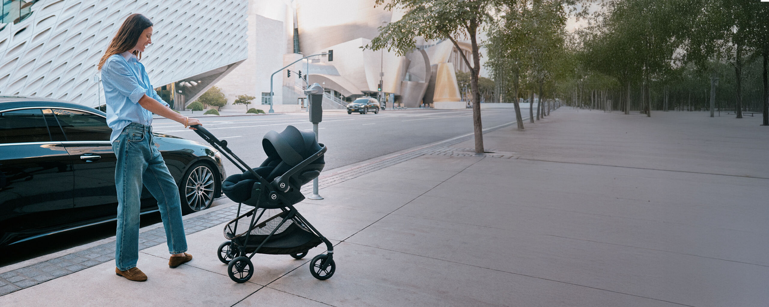 Una mamma che spinge un passeggino Melio Carbon con un seggiolino per neonati applicato.