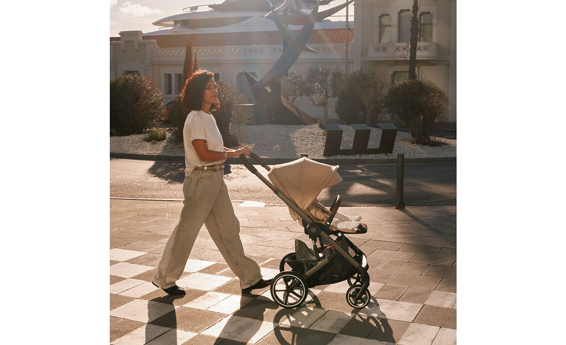 A woman pushing her Balios S Lux stroller with an attached seat pack, her child inside.