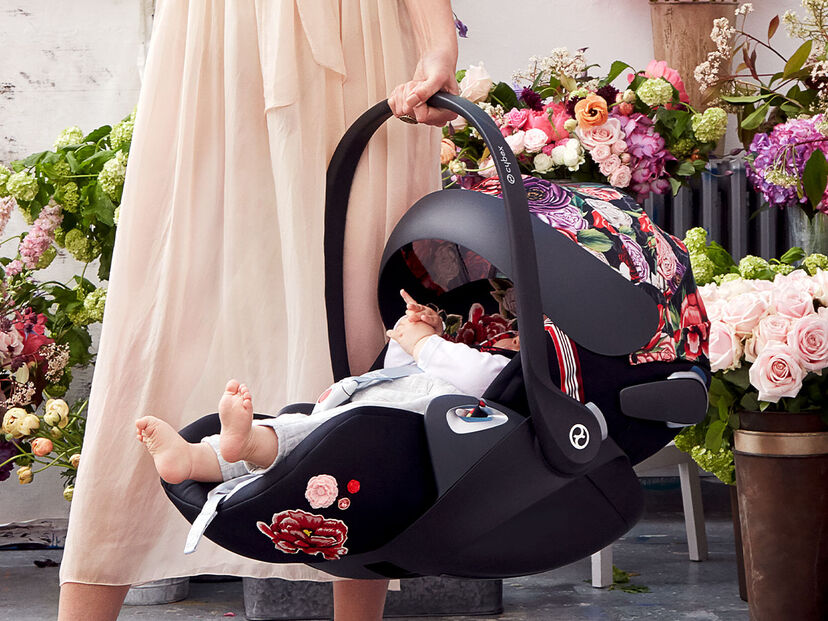 CYBEX Spring Blossom baby car seat with floral design, carried by a woman in a long dress, surrounded by flower arrangements.