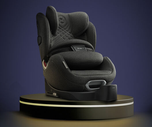 A modern dark grey child car seat on a pedestal against a dark blue background.