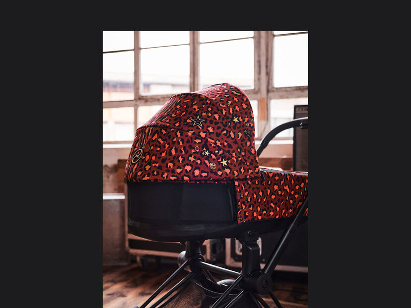 Kinderwagen CYBEX Rockstar mit rotem Leopardenmuster und goldenen Sternen in einem Raum mit gro&szlig;en Fenstern.