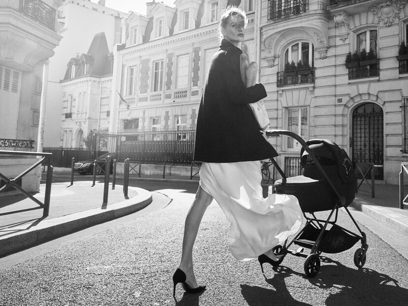 A stylish woman pushes a pram down a Parisian street while carrying a baguette.
