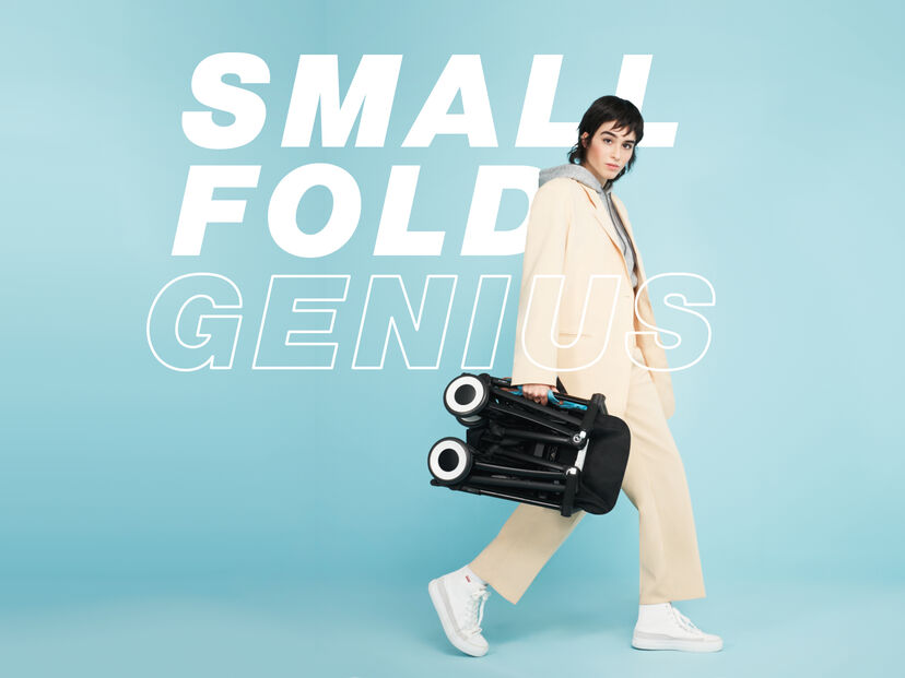 A person in a cream-colored suit carries a folded stroller against a blue background. The text "Small Fold Genius" is visible in the background.