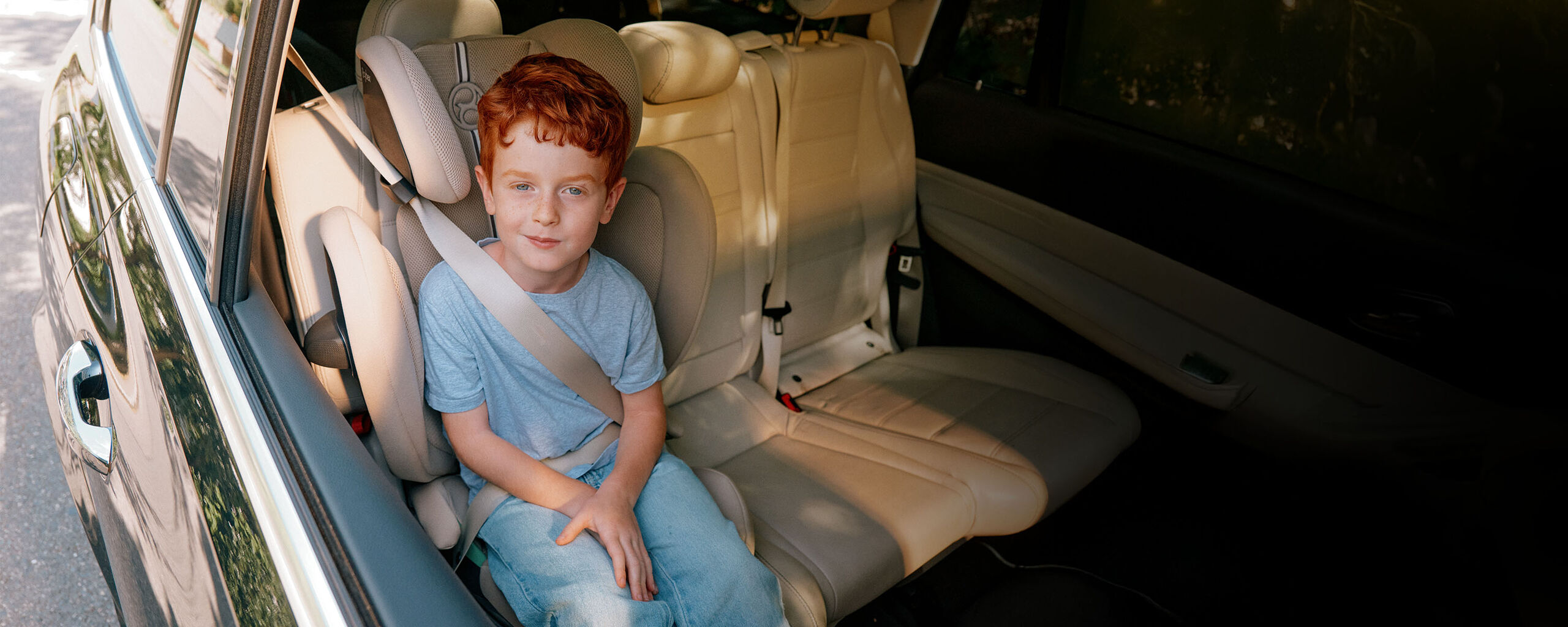 Een jongen met rood haar zit veilig in een auto op een kinderzitje met een veiligheidsgordel.