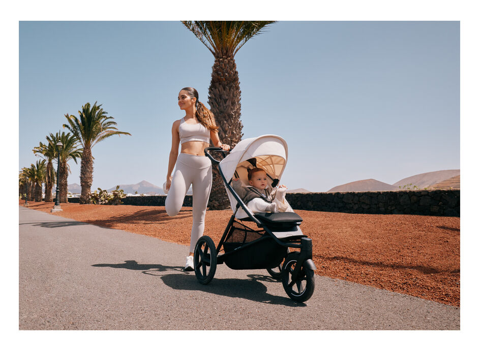A woman stretching, one hand on her Avi Spin pushchair with her child sitting inside.