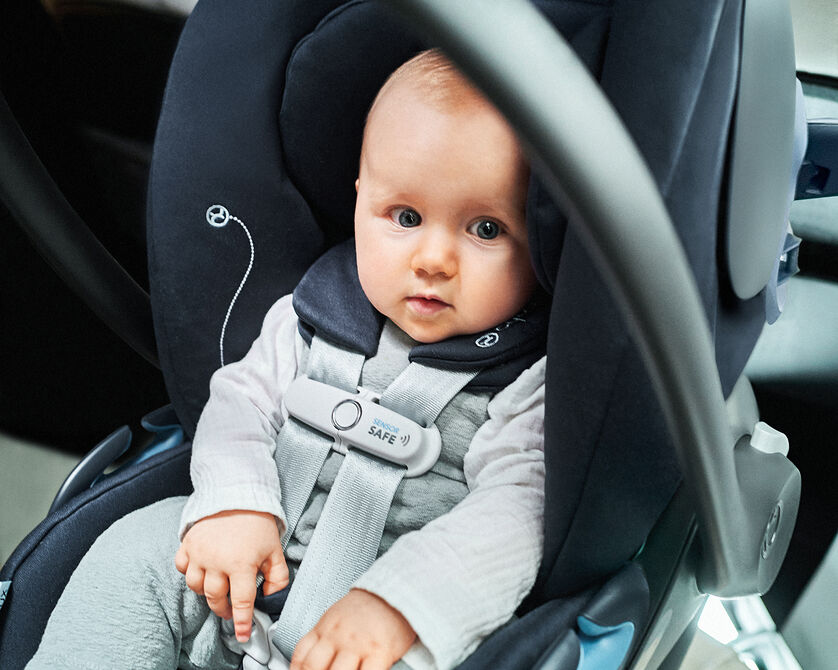 A baby sitting in a car seat with a safety harness.