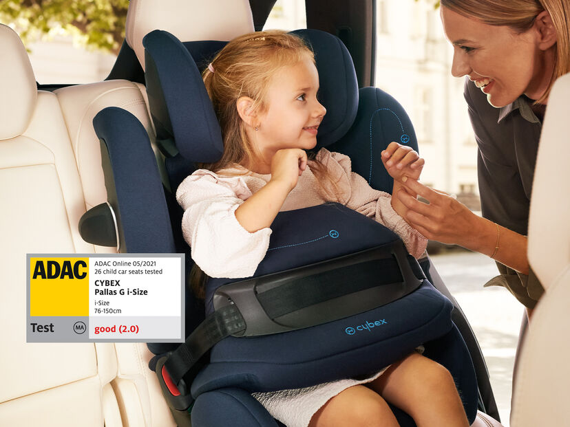 A young girl sits in a Cybex Pallas G i-Size car seat in a car, while a woman smiles and talks to her.