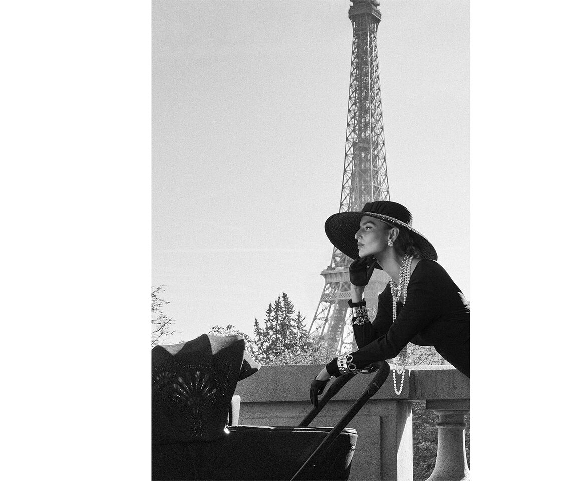Woman in elegant attire with a pram in front of the Eiffel Tower.