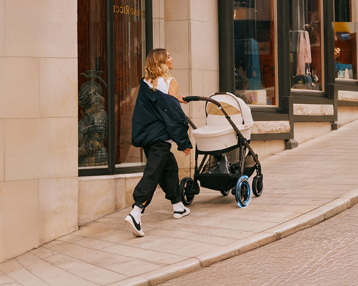 A woman pushing a pram up a cobbled street, dressed in a blue jumper and beige scarf.