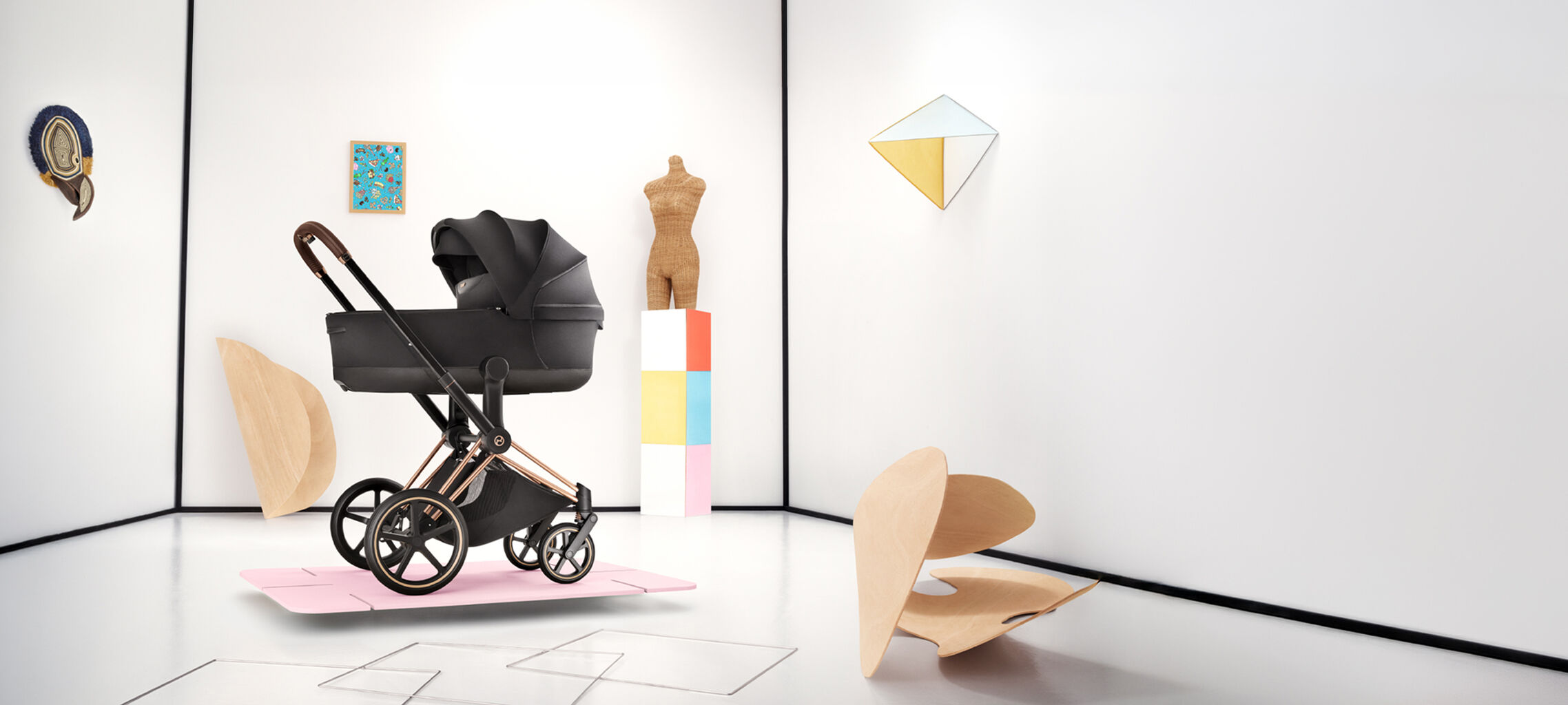 A Priam stroller on a pink thin platform. Various shapes and forms scattered behind and next to it.