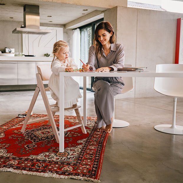 A woman and a young girl sitting at a table in a modern kitchen. The girl is seated on a Click and Fold high chair.