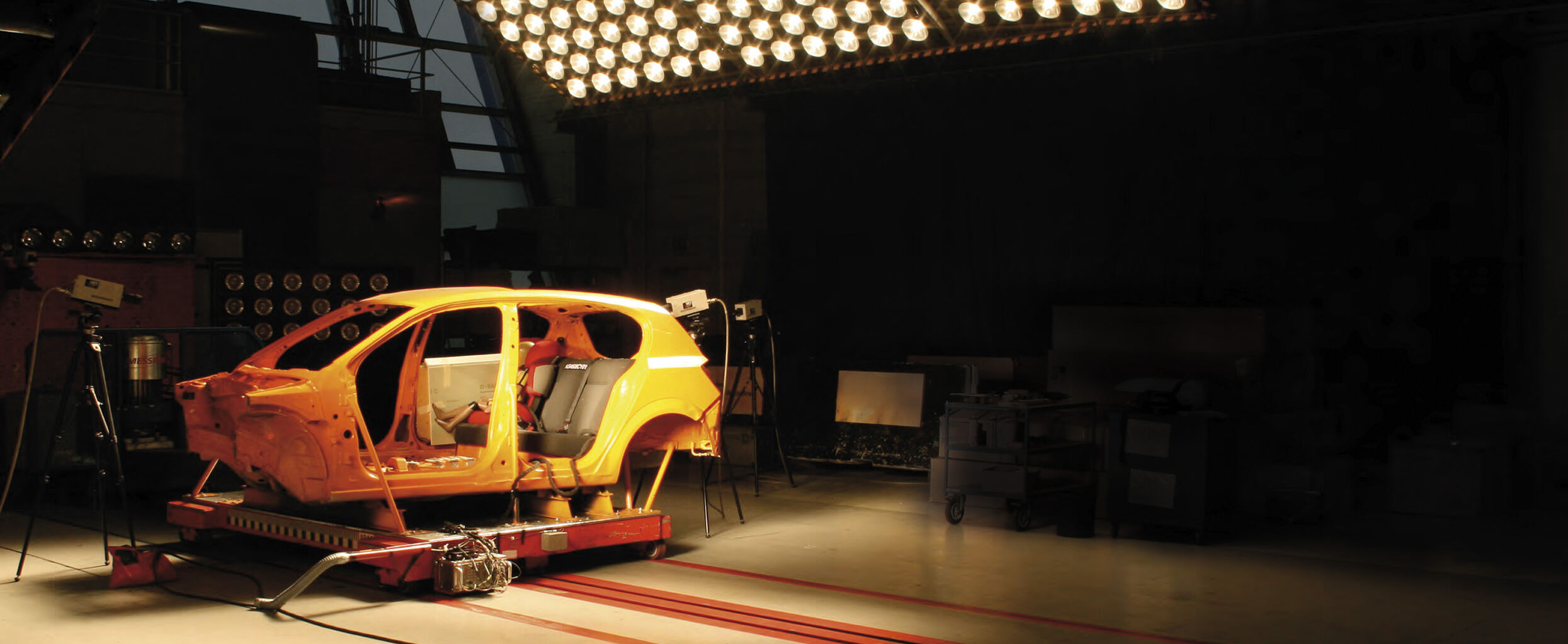 A yellow car shell on a test rig in a laboratory, surrounded by cameras and lighting.