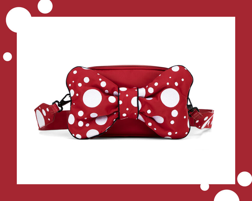 A red crossbody bag with a large bow and white polka dots on a red background.