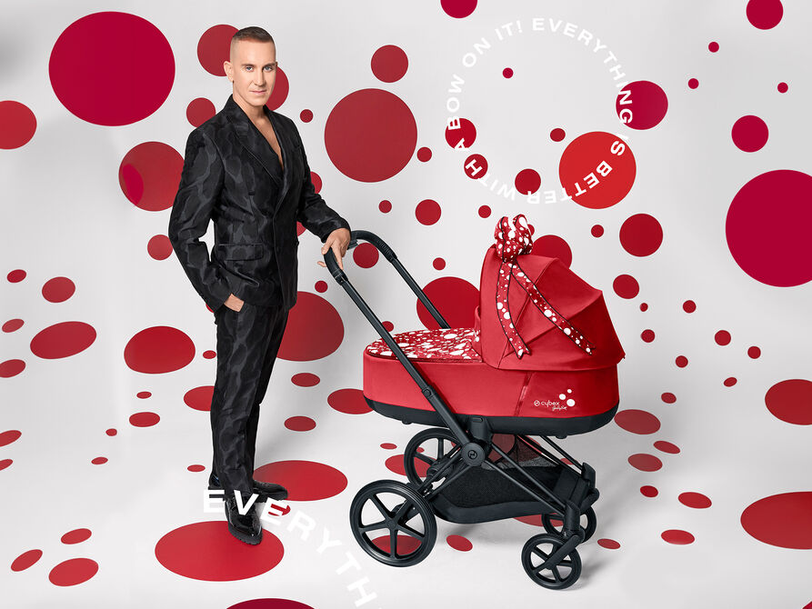 A stylish man in a black suit stands next to a playful red pushchair with white polka dots from the Petticoat by Jeremy Scott collection.