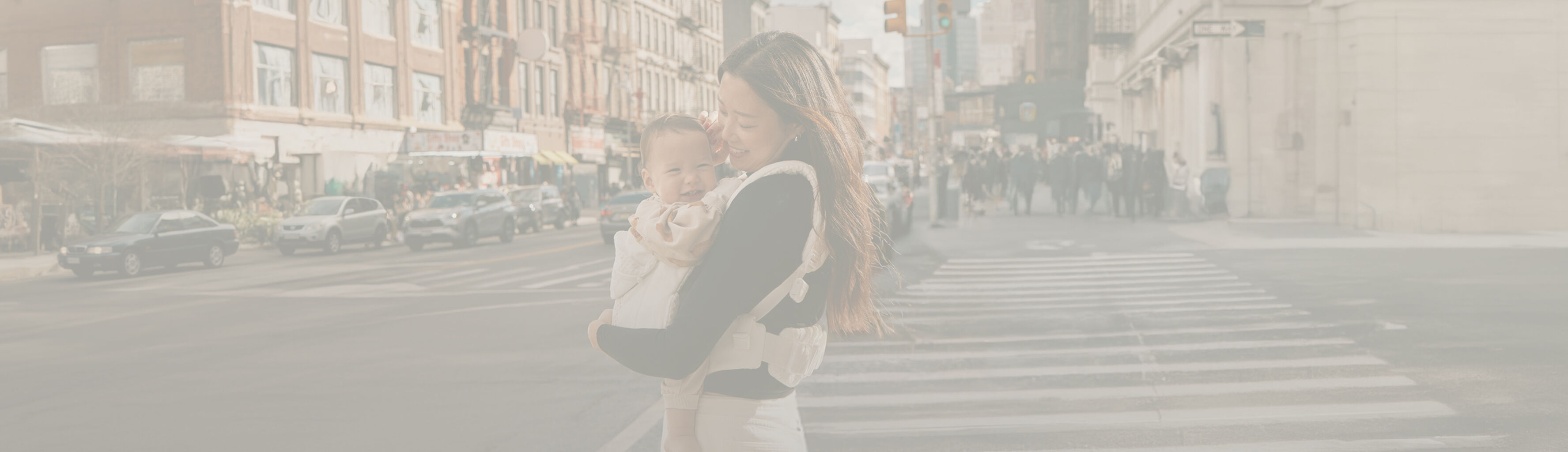 A woman standing on the streets of New York, smiling down at her baby in a baby carrier.