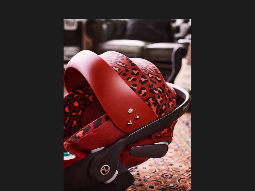 CYBEX Rockstar Kindersitz in Rot mit Leopardenmuster auf einem Teppich.