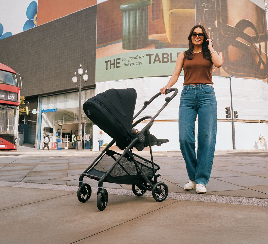 Woman wearing sunglasses pushing the Melio Carbon, a lightweight pushchair, in an urban square