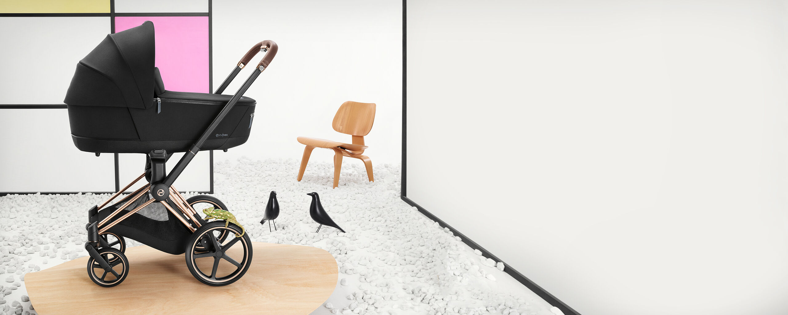 Pram in a modern room with a wooden chair and decorative birds on pebbles.