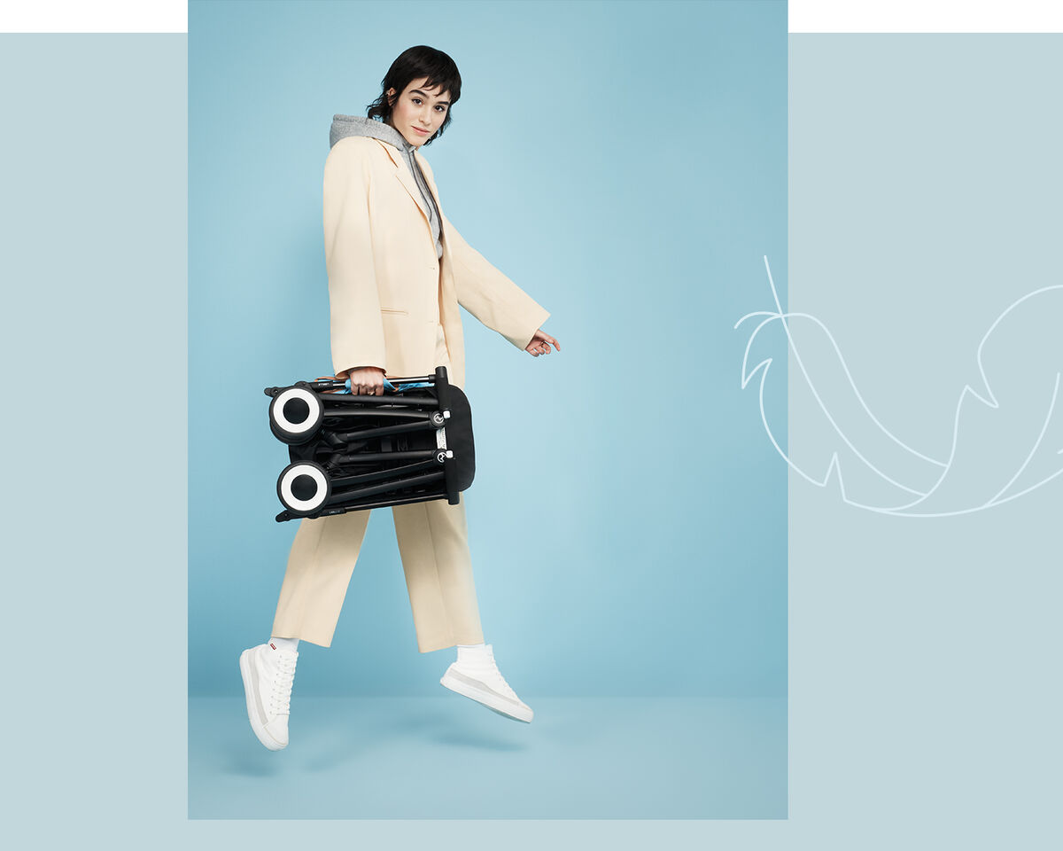 Person carrying a Libelle smallest fold stroller against a blue background.