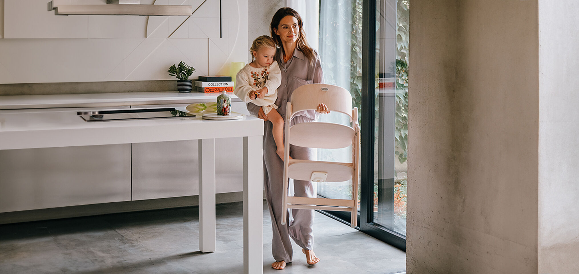 Mother carrying a child and a Click and Fold reclining infant car seat in a modern kitchen.