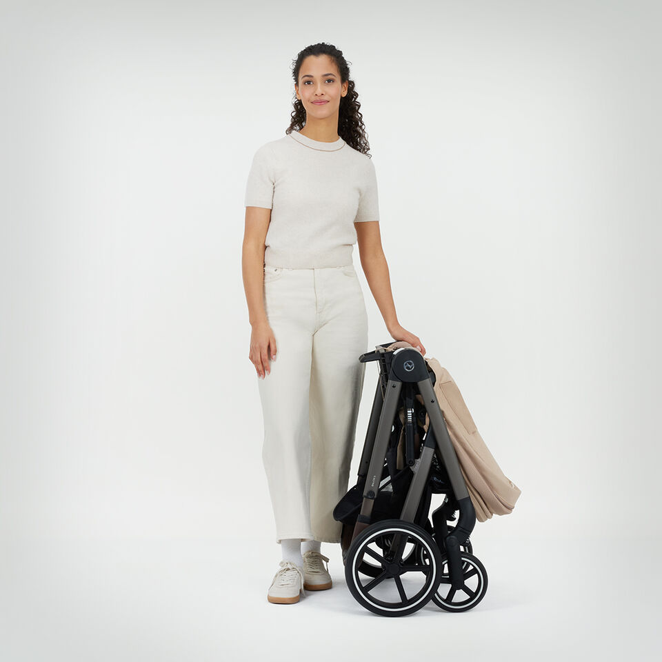 A woman standing next to a folded up Balios S Lux stroller. 