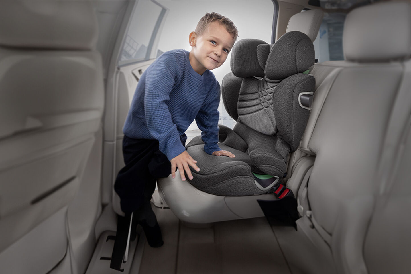 Un bambino con un maglione blu &egrave; in piedi su un seggiolino auto grigio.