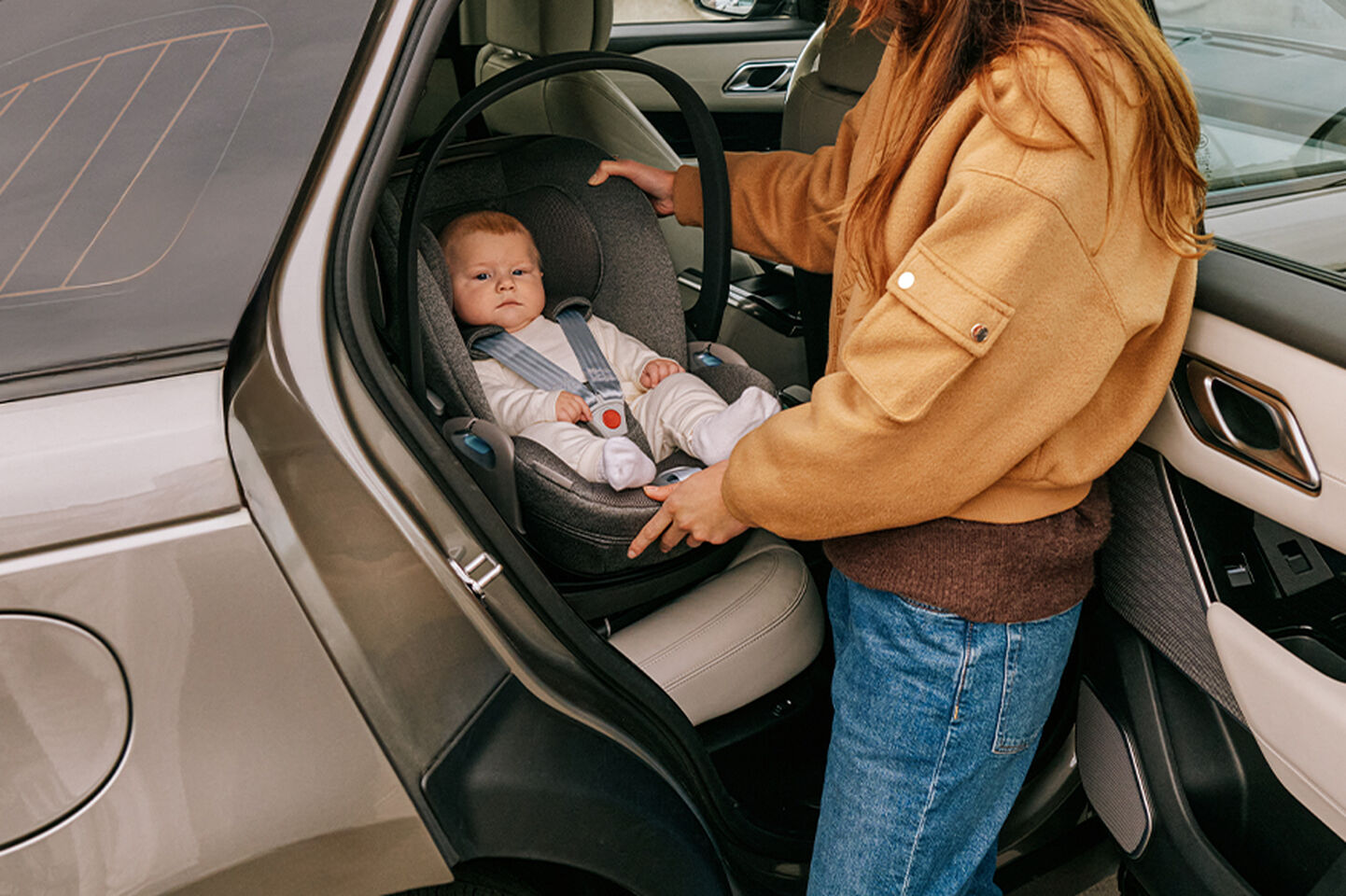 A parent is placing a baby into a car seat inside a vehicle with the door open.